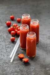Tomato juice in a tall glass bottle with a straw on a dark gray background