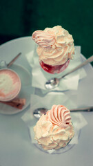 Strawberry ice cream dessert with whipped cream and crushed meringue, served in a glass cup. A cup of coffee on the coffee table.