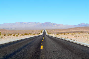 Fototapeta na wymiar Long Road in Desert - Two-Lane Highway With Blue Sky and Hills in Background