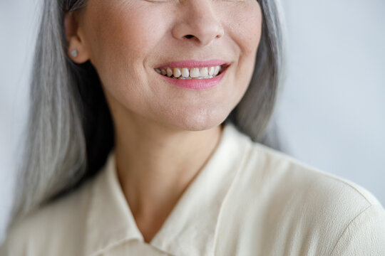 Positive mature lady in beige shirt smiles to camera showing healthy teath on light background in studio closeup