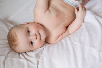 a cute baby is lying in diapers in a bed with white cotton bed linen. High quality photo