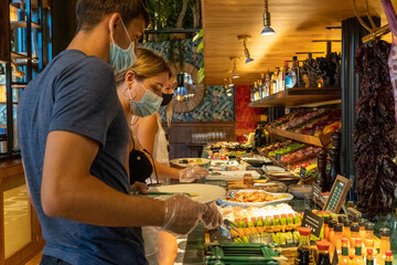 Caucasian friends with mask and plastic gloves having food in a self service restaurant