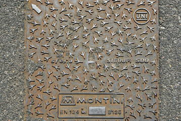 Close-up of a manhole cover with a decorative pattern, surrounded by the asphalt of a street, Italy
