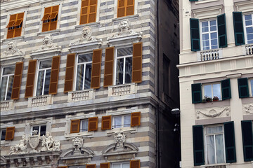 Facade of old houses with green and brown window shutters in historic part of Genoa city.