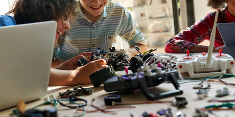 School kids boys helping building robotic car learning together at STEM class. Happy students...