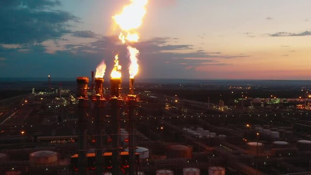 Flare stacks of the petroleum refinery are releasing fire at sunset
