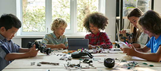 Multiracial school kids students making robotic cars using tablet computer. Diverse junior children...