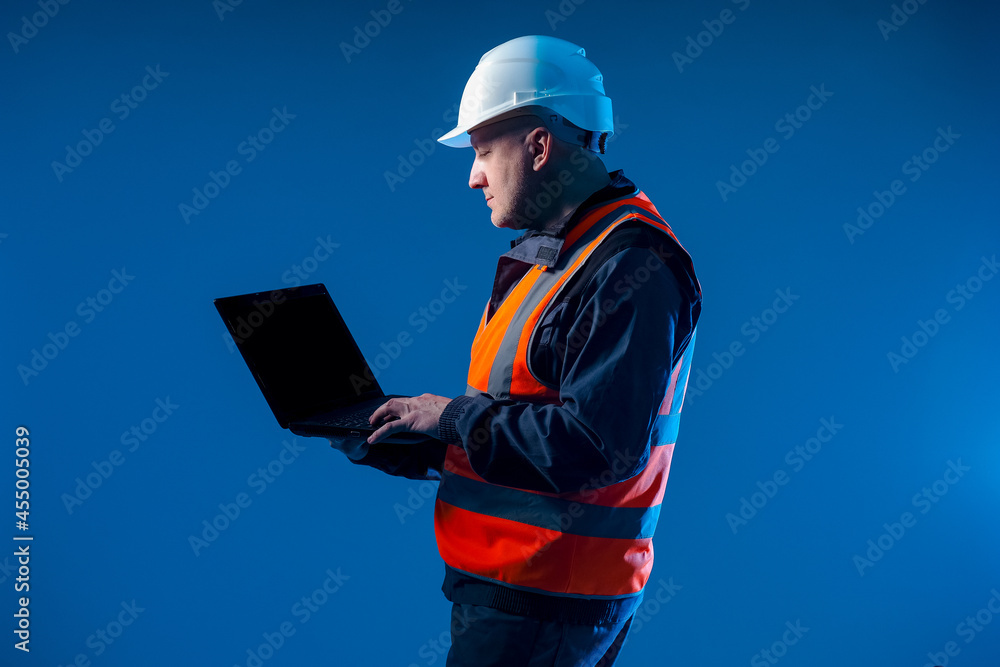 Poster portrait of a builder engineer. engineer in a working uniform holds a laptop. builder on dark blue b