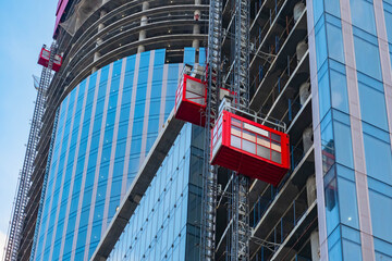 Construction site with elevator lift. Glass skyscraper with elevator for workers. Construction skyscraper. Buildings residential under construction with a red elevator. Skyscraper erection. © Grispb