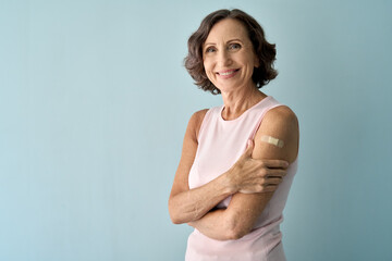 Smiling healthy mature older senior happy woman showing bandage on arm after getting vaccination....