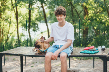 Funny french puppy bulldog and teenager playing games outside. Adorable orange bulldog in blue harness in the playground on a sand. Still life, friendship with a dog.