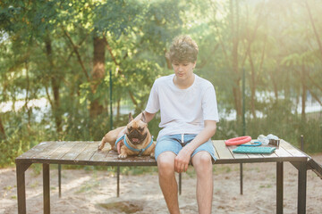 Funny french puppy bulldog and teenager playing games outside. Adorable orange bulldog in blue harness in the playground on a sand. Still life, friendship with a dog.