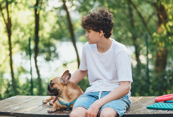 Funny french puppy bulldog and teenager playing games outside. Adorable orange bulldog in blue harness in the playground on a sand. Still life, friendship with a dog.