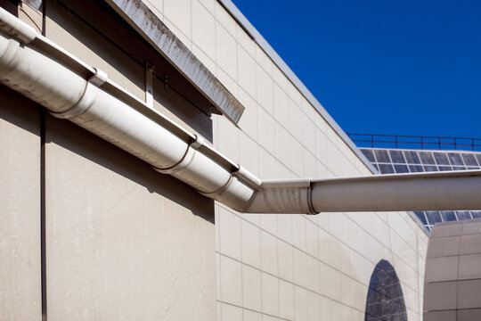 drainage gutter to drain rainwater from the roof of a house facade tiled on a sunny day exterior close-up.