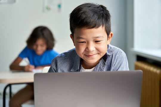 Happy smiling Asian school boy using laptop computer at class in classroom. Smiling chinese junior school student learning online virtual education digital program app technology during tech lesson.