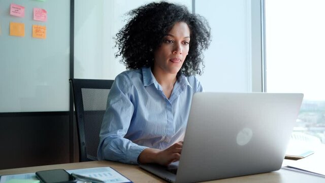 Young African American focused female executive manager businesswoman sitting at desk working typing on laptop computer in contemporary corporation office. Business technologies concept.