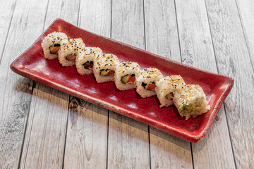 red porcelain tray with uramaki sushi california roll with sesame seeds stuffed with salmon, nori seaweed and cream cheese