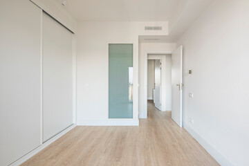 Bedroom with white built-in wardrobe, ducted air conditioning, white wood carpentry, oak-colored parquet flooring
