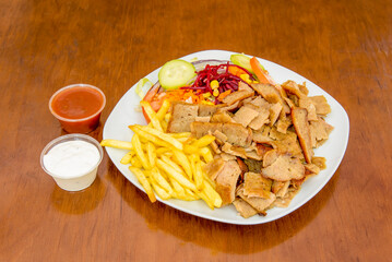 Kebab menu on plate with fried potatoes, chopped roast lamb doner, beetroot, carrot, cucumber and red onion salad with red and white sauce
