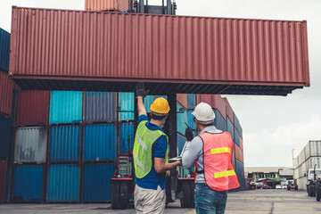 Industrial worker works with co-worker at overseas shipping container yard . Logistics supply chain management and international goods export concept . - obrazy, fototapety, plakaty