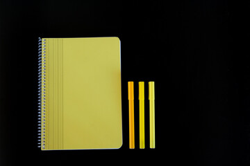 Yellow notebook and pens on black background