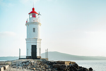 Fototapeta na wymiar An old lighthouse with a red roof on the seashore. Seascape with copy space. Postcard from travel.