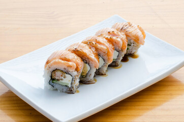 Sushi rolls with teriyaki salmon on white plate on wooden table