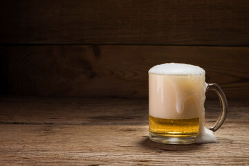 Beer glass with white beer foam on a dark wooden table background