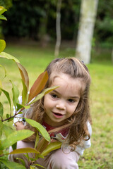 menina de 2 anos de idade, cabelos compridos, beincando feliz no jardim. Diversão de criança.