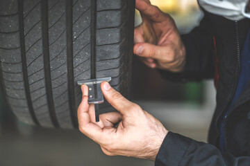 Mechanic checking checking the depth of car tire tread.  Car maintenance and auto service garage...