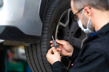 Mechanic checking checking the depth of car tire tread.  Car maintenance and auto service garage concept.