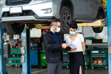 Mechanic man and woman customer wearing medical face mask protection coronavirus and check the car condition before delivery.