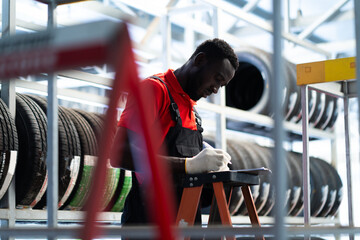 Black male mechanic choose car tire at a tire store. Expertise mechanic working in automobile...