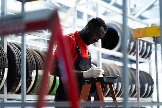Black male mechanic choose car tire at a tire store. Expertise mechanic working in automobile repair garage.