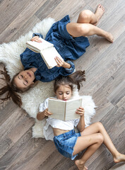 Little girls sisters read books lying on the floor, top view.