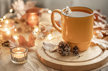 Cozy composition with a cup of tea, candles and autumn leaves.