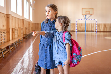 Little girls with backpacks in an empty school gym.