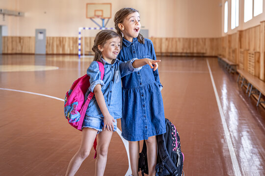 Little girls with backpacks in an empty school gym.