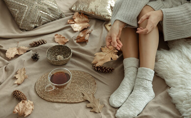 Autumn background with warm socks on female legs and a cup of tea in bed.