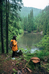 woman hiker with backpack in yellow raincoat looking at mountain lake