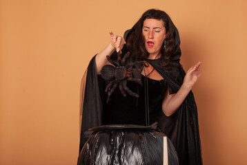 A black European woman in the role of a witch looks frightened into the cauldron for Halloween