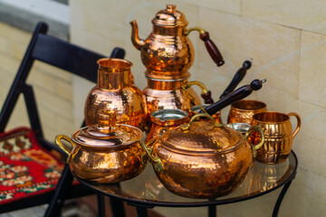 A set of bright copper dishes stands on a round glass table