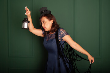 woman vamp on Halloween on a green background with a black lantern in her hands on Halloween, a...