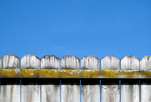 The top of an old fence with palings and blue sky background with copy space