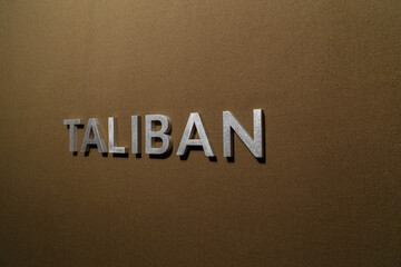 the word taliban laid with silver metal letters on rough tan khaki canvas fabric