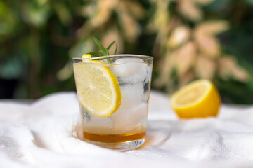Iced honey lemon soda with rosemary. Refreshment healthy drink with warm sunlight in a garden.