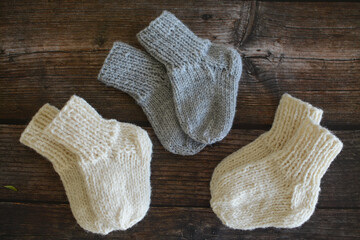 Fototapeta na wymiar Hand knitted baby socks, made of organic sheep wool yarn, on dark wooden background, vintage style