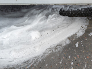 Soap sud waste flows to floor drain grid in car washing garage. Full frame close-up with selective...