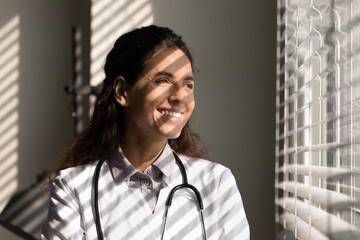 Happy satisfied medical professional looking out of window at morning sun, thinking of patients rehabilitation, future vision, career of doctor, feeling joy about promotion, Head shot portrait