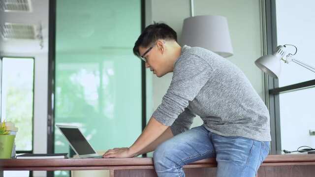 Stressed young asian businessman sit on desk with laptop computer thinking and typing on keyboard Disappointed from bad news or problem in working close laptop work from home quarantine. head on hand